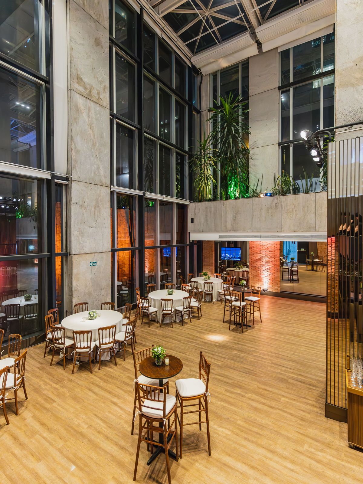 Tall glass-walled atrium venue set with round tables and an open dance floor