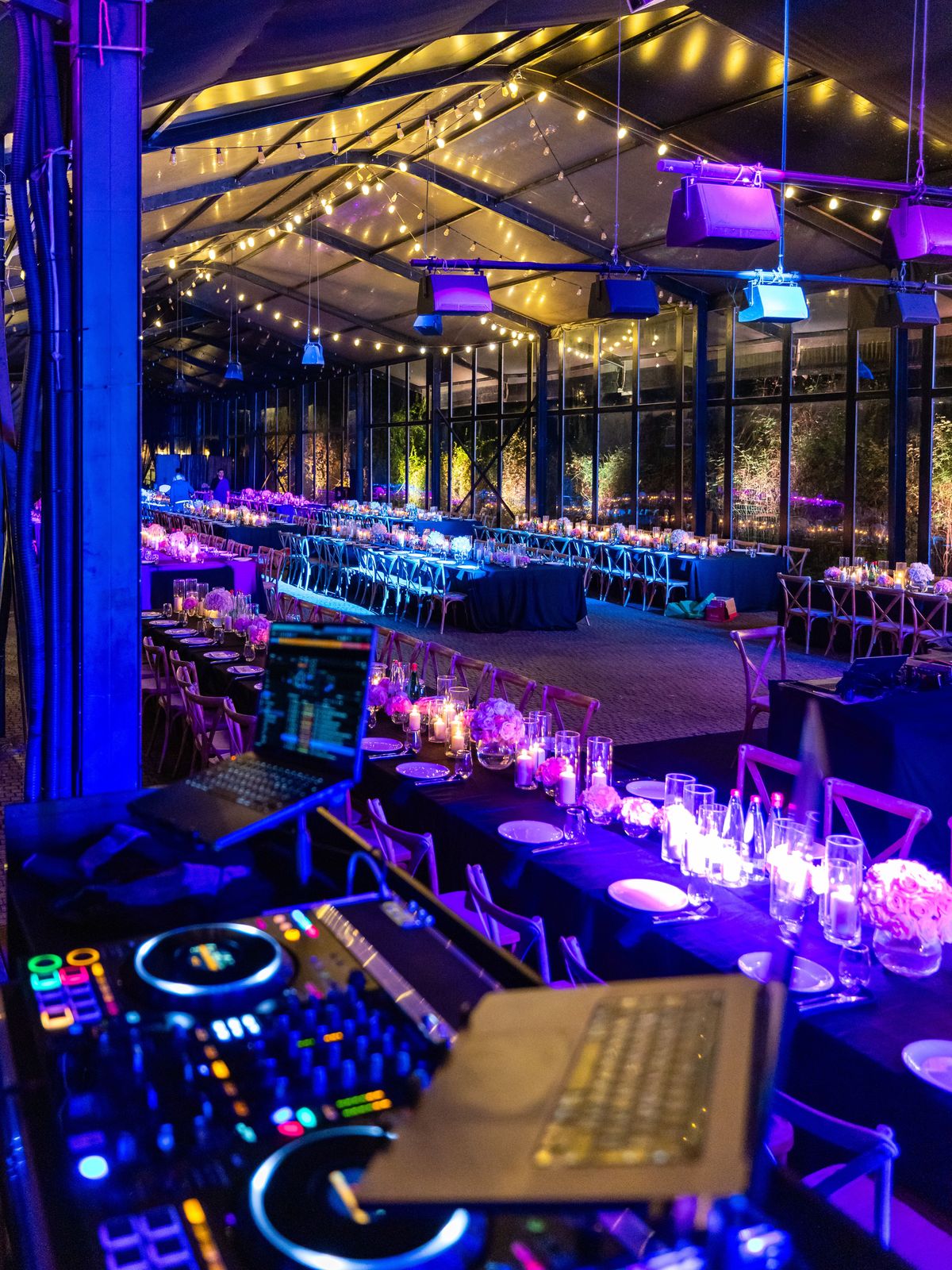 Reception tent washed in purple uplighting, the DJ booth in the foreground