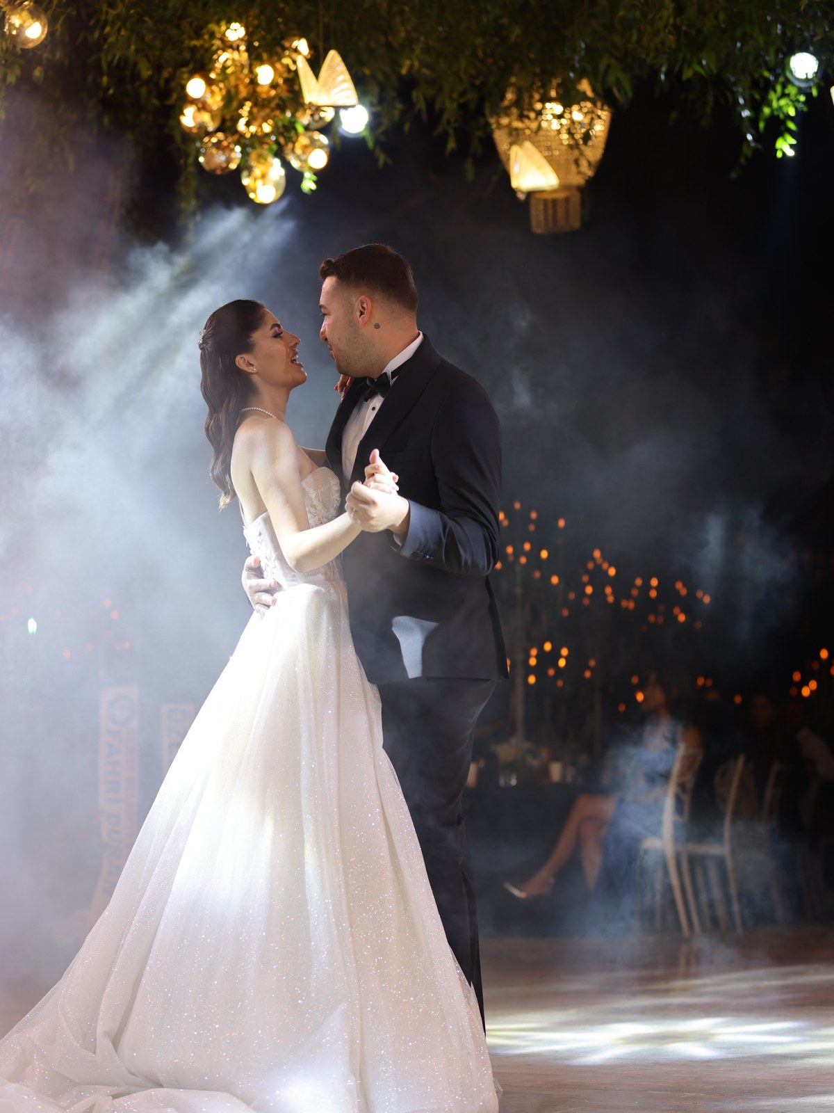 Bride and groom in a first dance, beams of light cutting through the haze